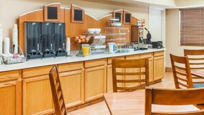 A breakfast bar with coffee machines, a fruit bowl, and a waffle maker.