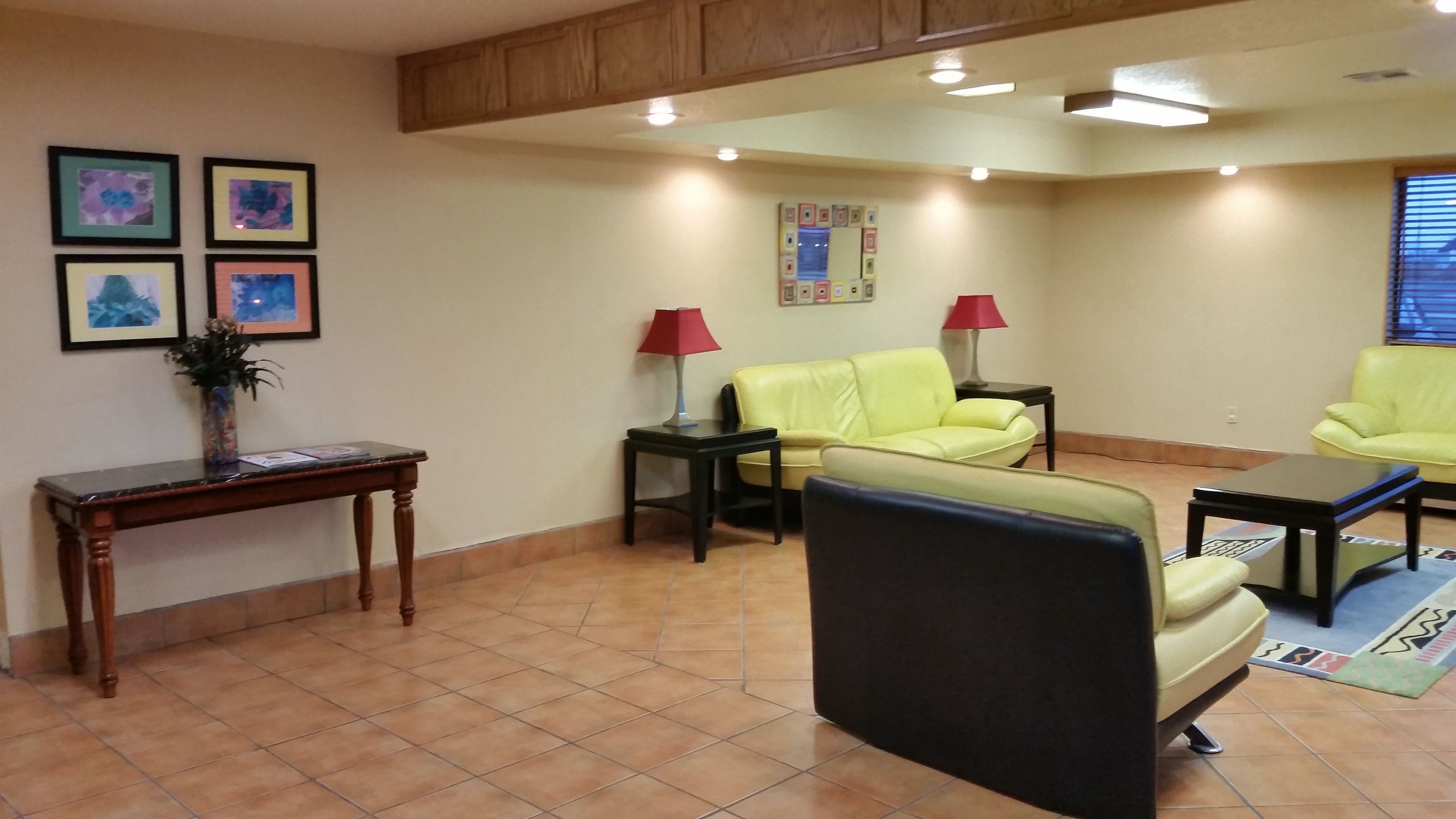 A waiting area with a wooden reception desk, two chairs, a small table, and a wall with framed pictures.