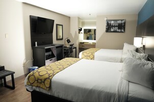 Habitación de hotel con dos camas, un escritorio, televisor, espejo y un cuadro en la pared.