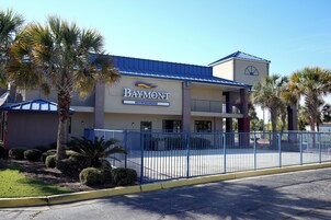 Edificio del Baymont Inn & Suites con techo azul, estacionamiento cercado y palmeras.