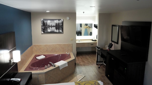 A bathroom with a large bathtub, a mirror, a sink, and a television. - Baymont by Wyndham Manning (Manning)