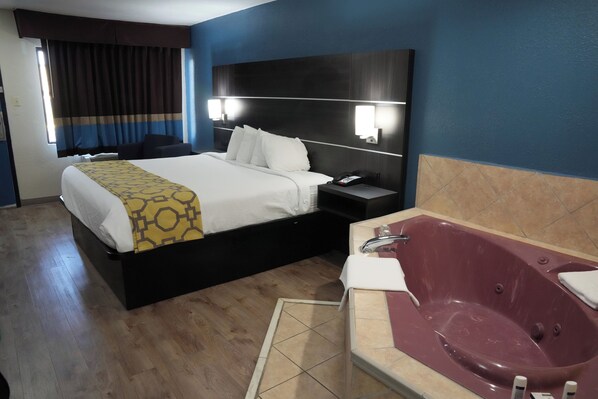Una habitación de hotel con cama, mesita de noche y una bañera grande.