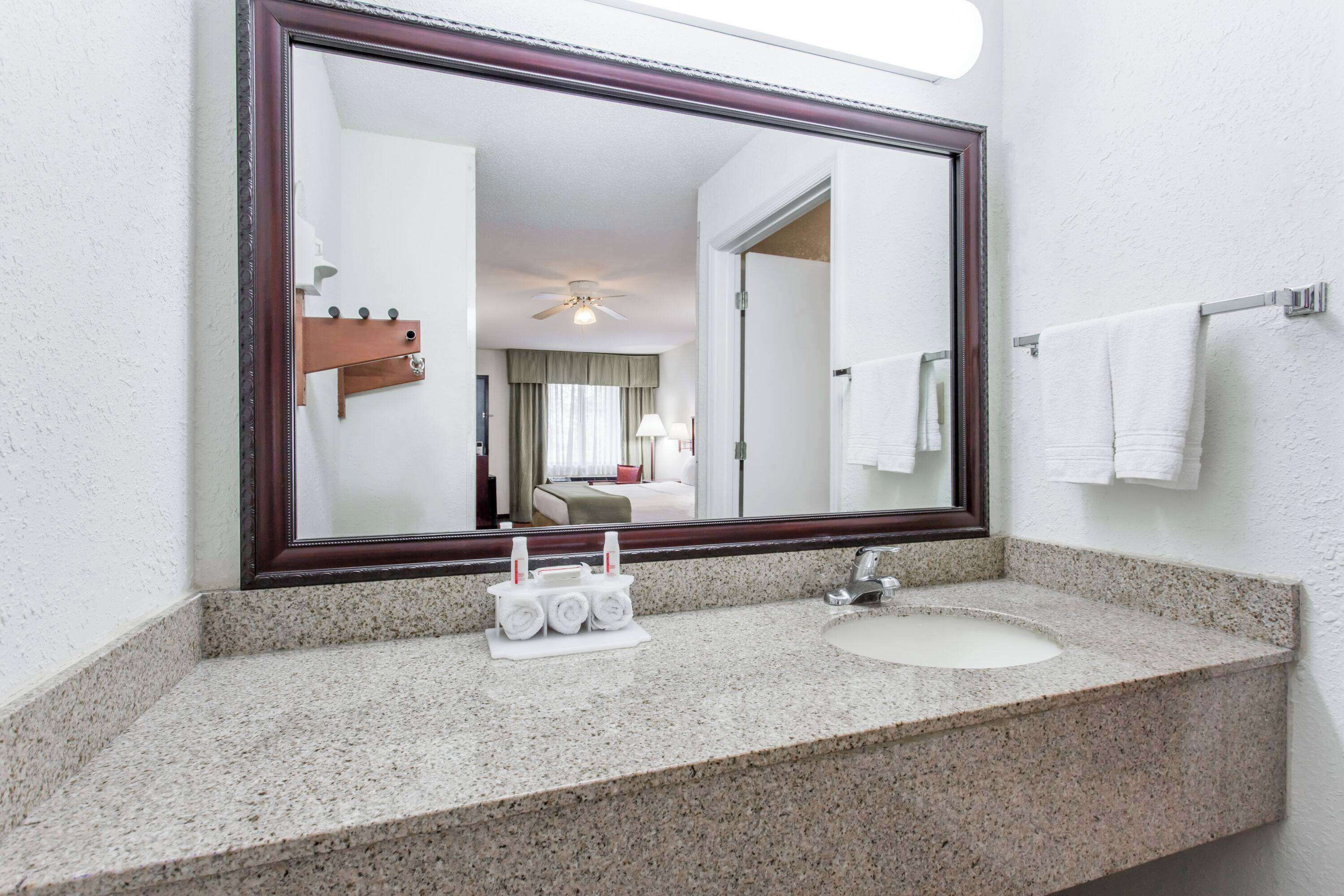 Un baño con un espejo grande, encimera de granito y un lavabo.