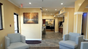 A reception area with two grey armchairs, a wooden floor, and a painting of a tree-lined path on the wall. - Baymont by Wyndham Manning (Manning)