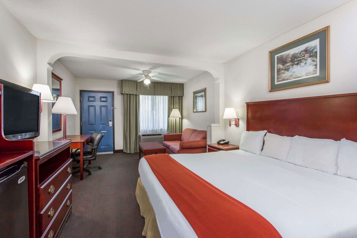 A hotel room with a bed, desk, chair, television, and a ceiling fan.