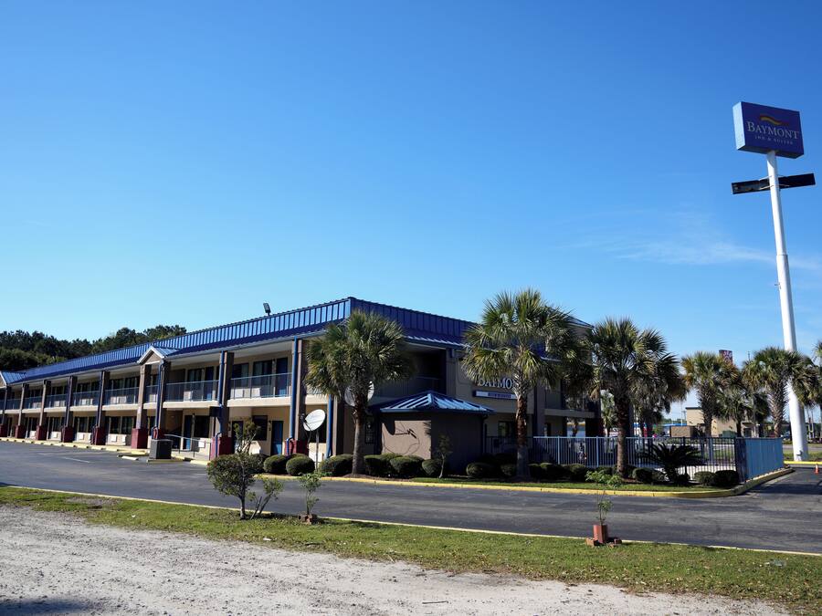 Un motel con tetto blu e diversi piani, circondato da palme e un cielo sereno.