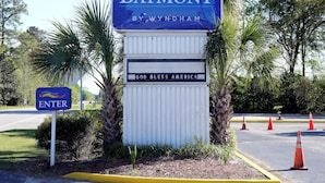 A sign for Baymont by Wyndham with a 'God Bless America' plaque, surrounded by greenery and traffic cones. - Baymont by Wyndham Manning (Manning)