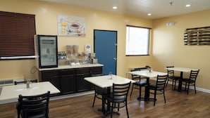 A dining area with tables and chairs, a counter with food items, and a door. - Baymont by Wyndham Manning (Manning)