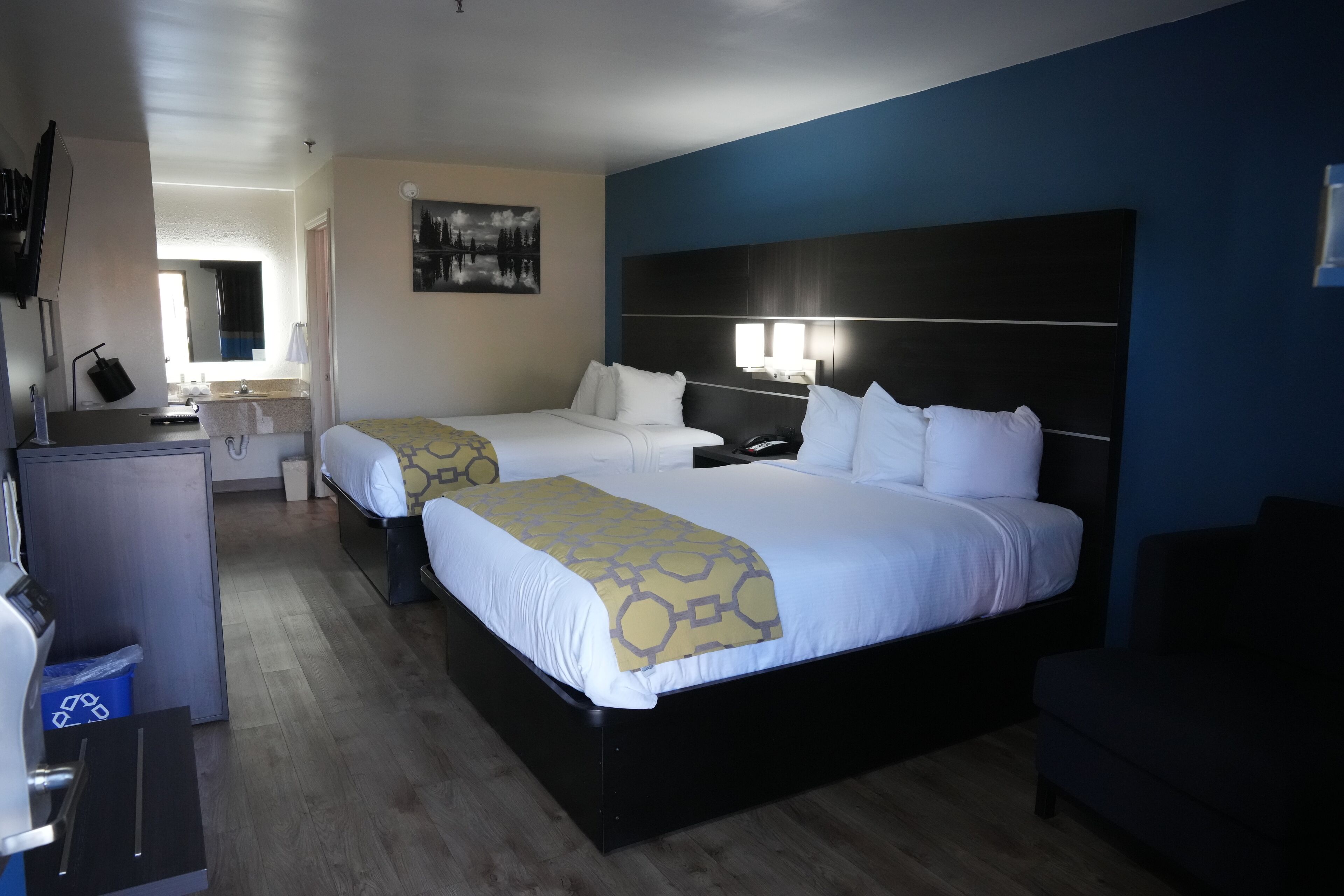 Ett hotellrum med två sängar, ett skrivbord, en spegel och en tavla på väggen.