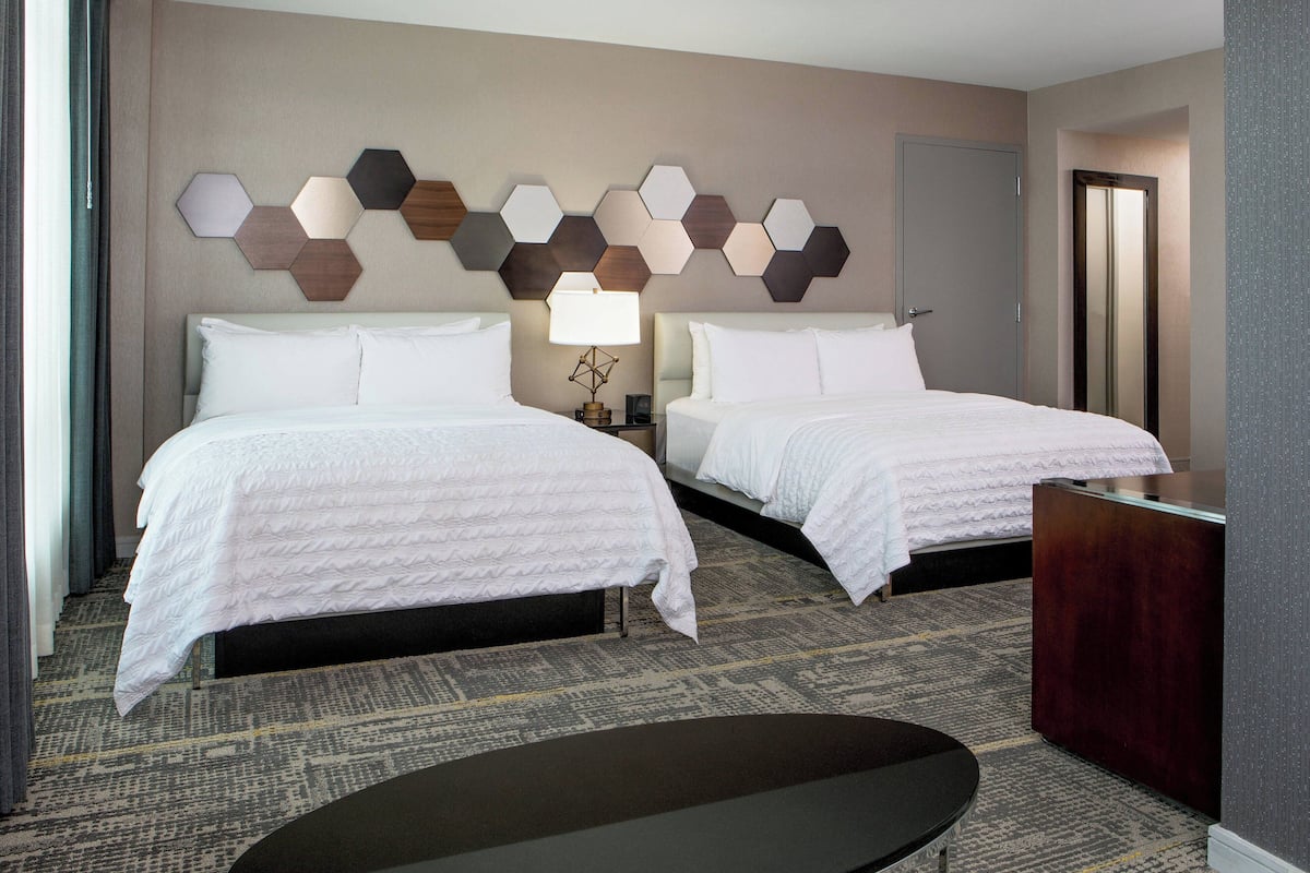 A hotel room with two beds, a desk, a lamp, and a decorative wall panel.