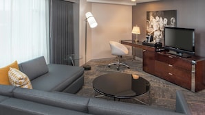 A modern hotel room with a grey sofa, a small round table, a desk with a television, and a large window with curtains. - Le Méridien Boston Cambridge (Cambridge)