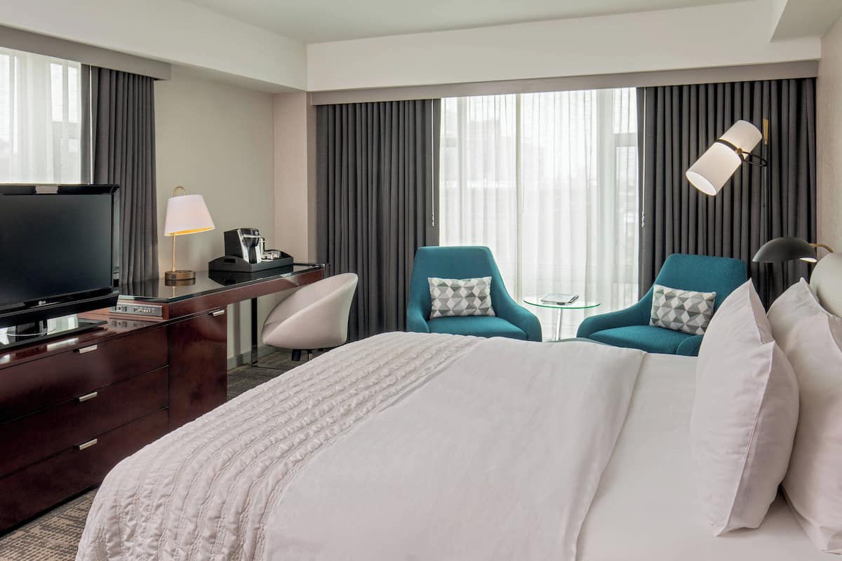 A hotel room with a large bed, two armchairs, a desk with a TV, and a lamp.