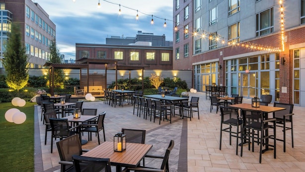 An outdoor patio area with multiple tables and chairs, string lights, and a well-maintained lawn. - Le Méridien Boston Cambridge (Cambridge)
