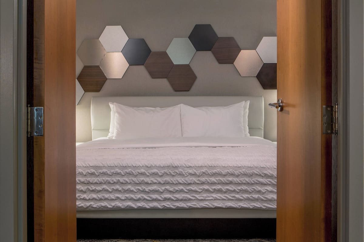 A hotel room with a bed, a wooden door, and a wall with hexagonal panels.