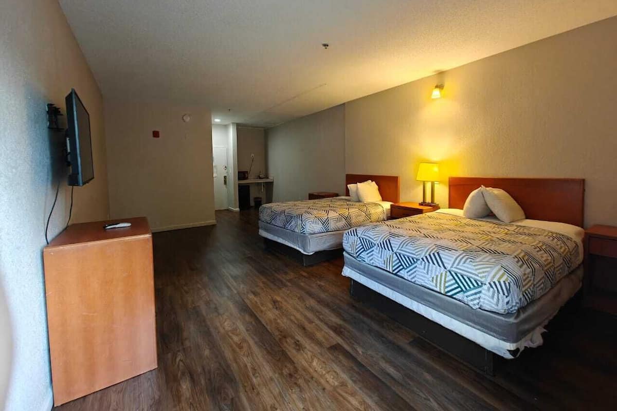 A hotel room with two beds, a wooden desk, a TV, and a small kitchenette.