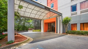 A modern building entrance with a covered walkway, a clear sky, and a parking area. - Budgetel Inns & Suites - Atlanta Galleria Stadium (Atlanta)