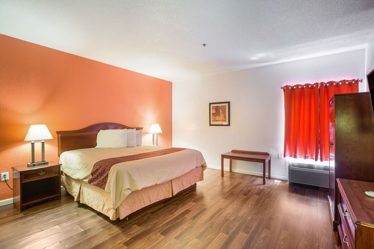A hotel room with a bed, bedside tables, a desk, a chair, a TV, and a window with curtains.