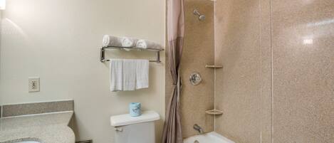 A bathroom with a toilet, sink, and bathtub. There is a towel rack with towels and a shower curtain.