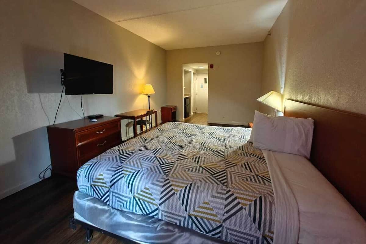 A hotel room with a bed, a desk, a chair, a TV, and a lamp.