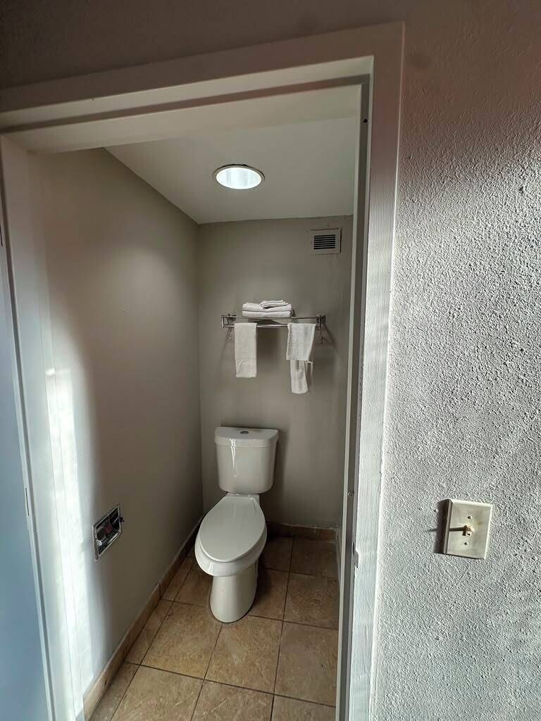 A small bathroom with a toilet, a shelf with towels, and a light fixture on the ceiling.
