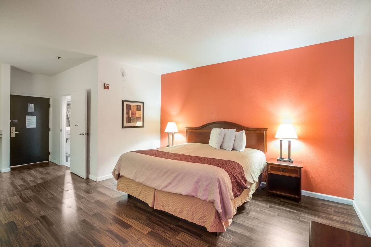 A hotel room with a large bed, two bedside tables with lamps, a wooden floor, and an orange accent wall.