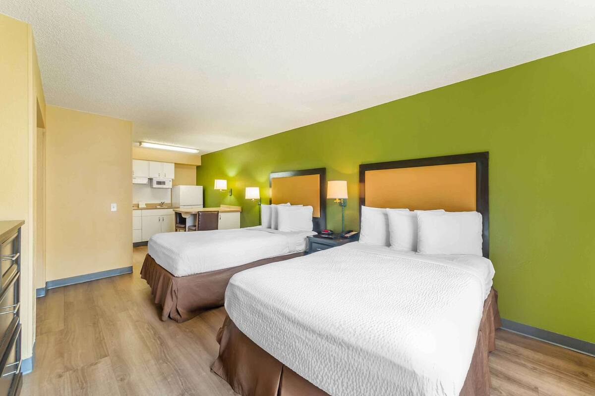 A hotel room with two beds, a kitchenette, and a green accent wall.