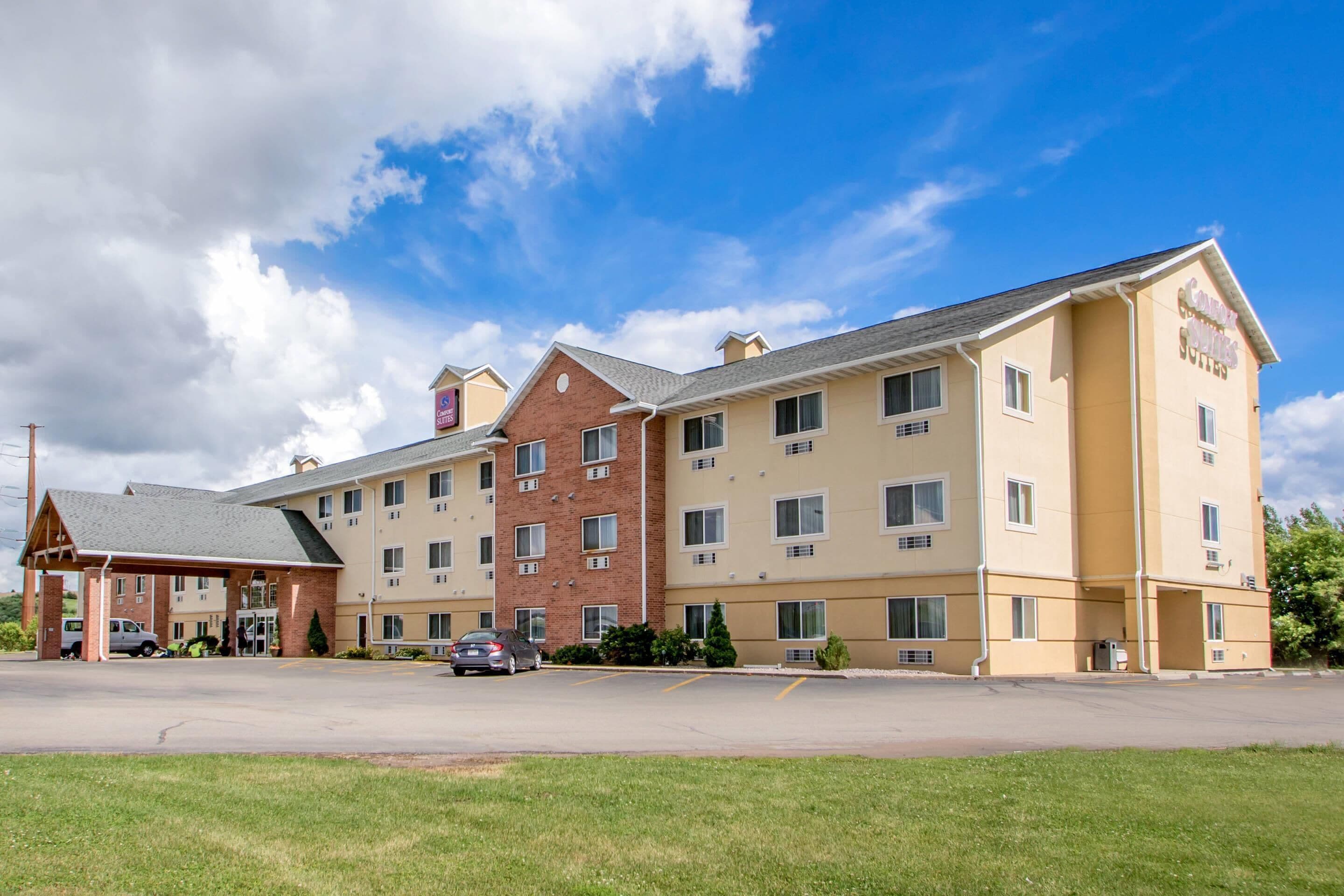 A multi-story hotel with a central courtyard, parking lot, and a clear blue sky.
