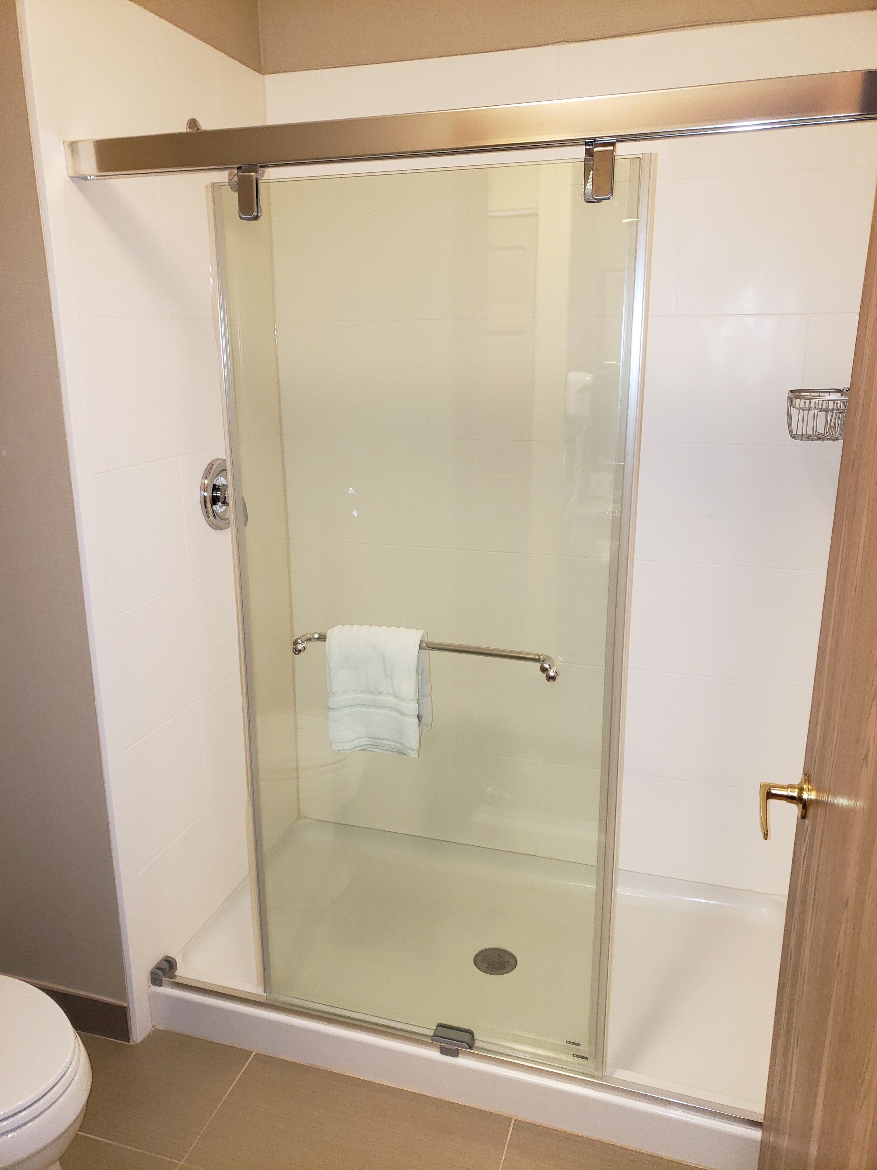 A glass-enclosed shower stall with a towel rack, a visible drain, and a door with a brass handle.