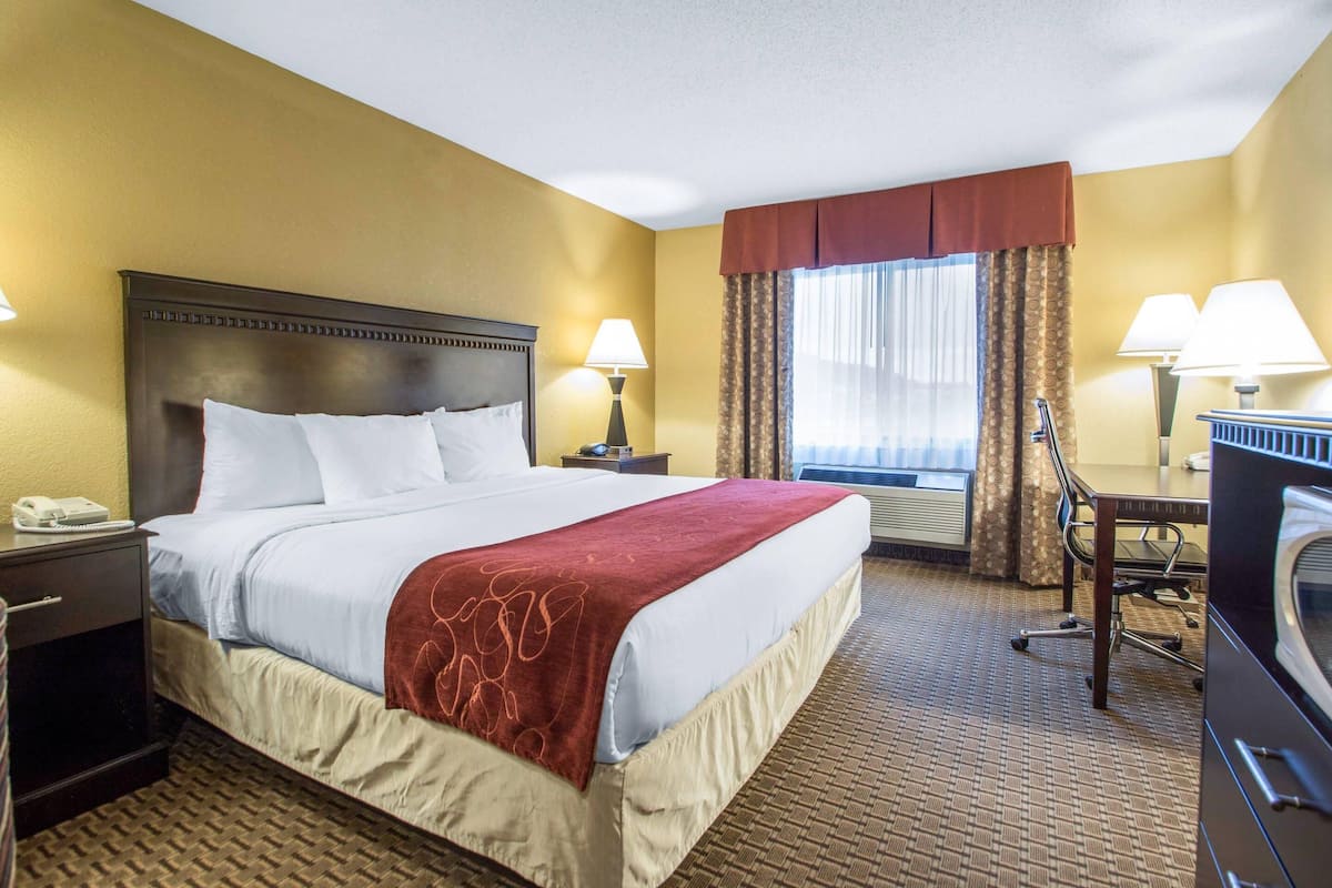 A hotel room with a large bed, two bedside lamps, a desk with a chair, a telephone, and a window with curtains.
