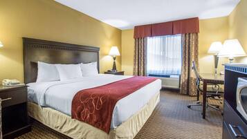A hotel room with a large bed, two bedside lamps, a desk with a chair, a telephone, and a window with curtains.