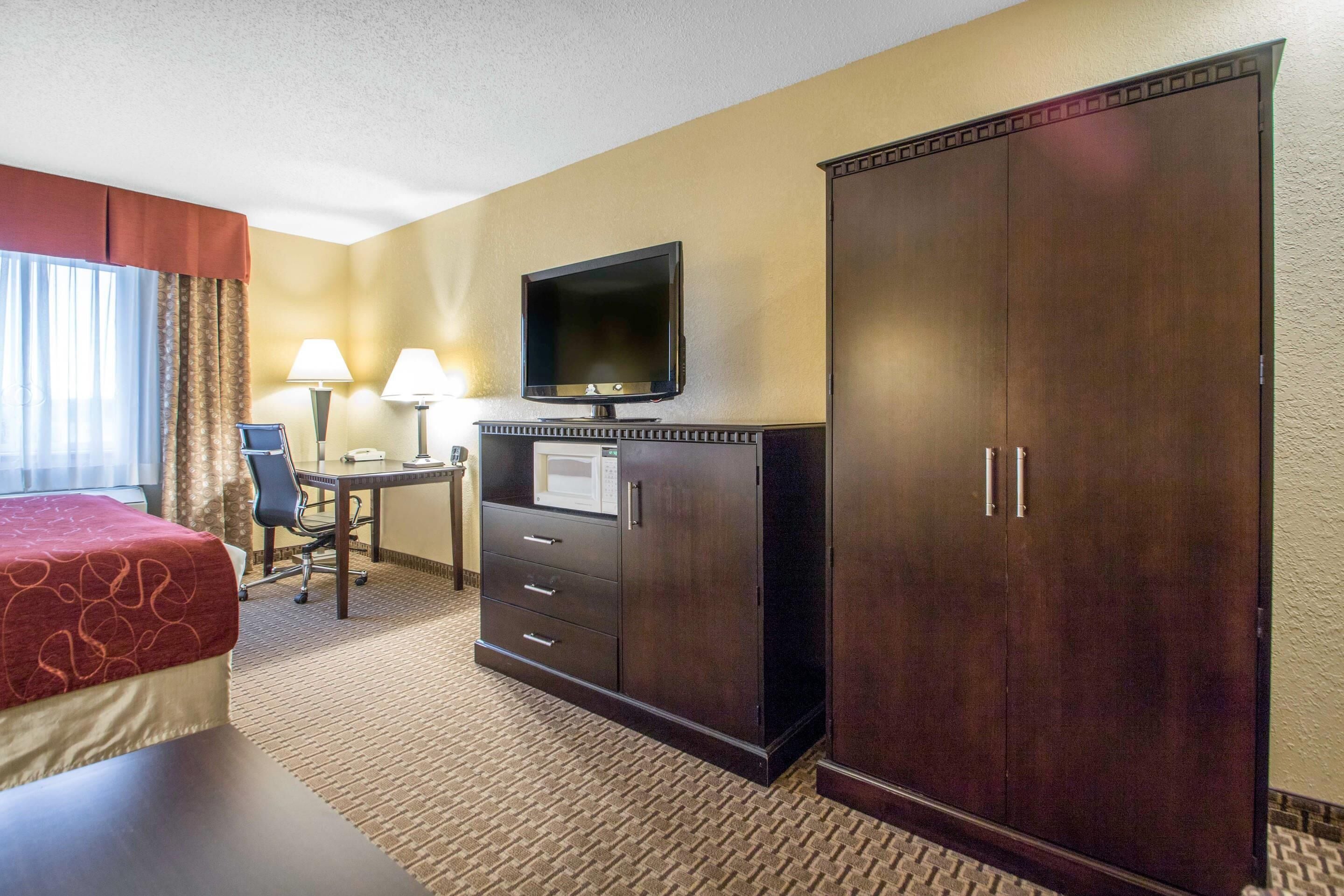 Quarto de hotel com cama, escrivaninha, televisão e guarda-roupa.