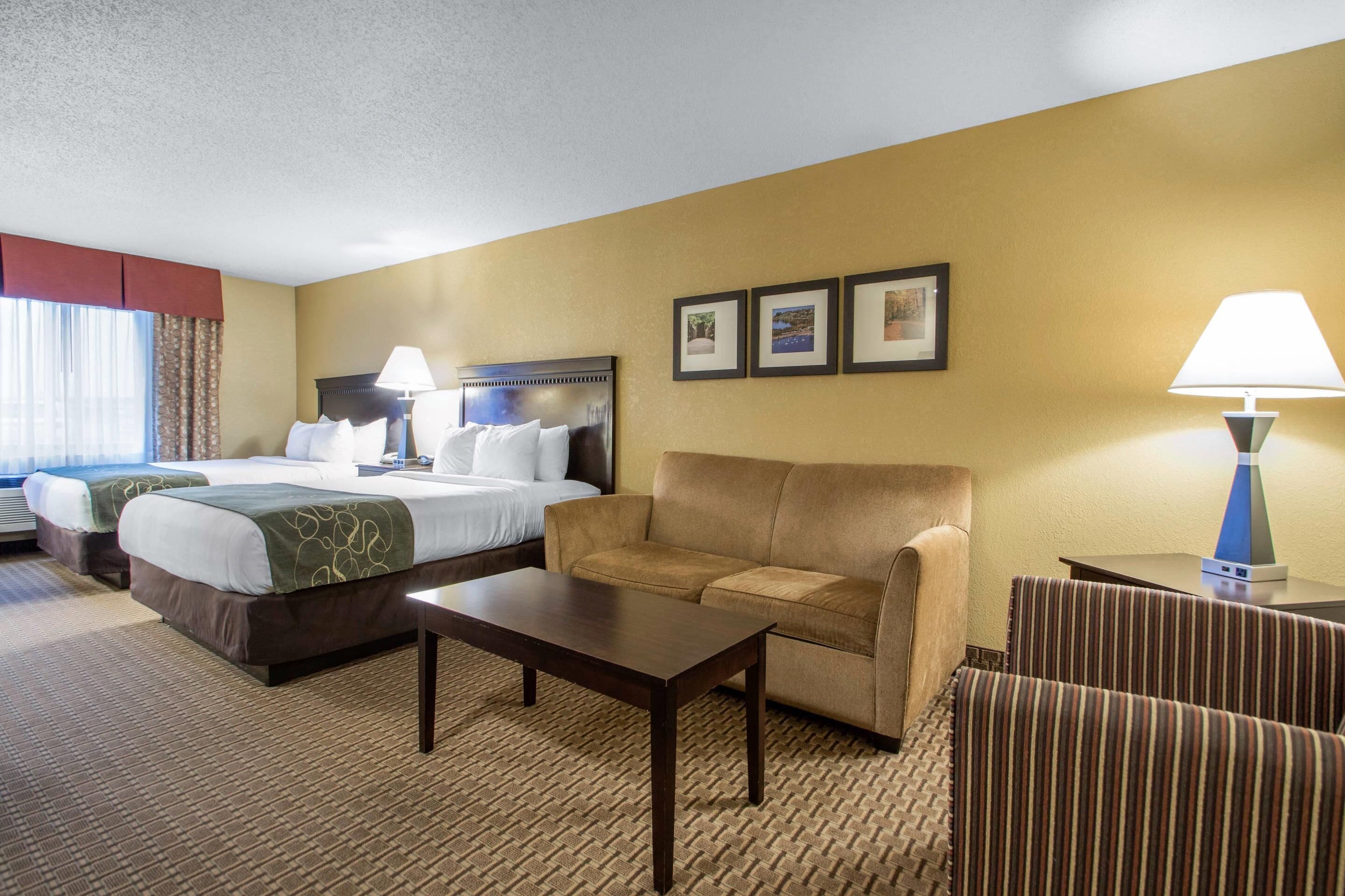 A hotel room with two beds, a sofa, a coffee table, and a lamp.