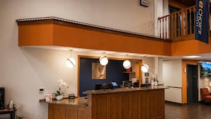 Un espace d’accueil d’hôtel avec un comptoir en bois, un écran numérique et un drapeau.