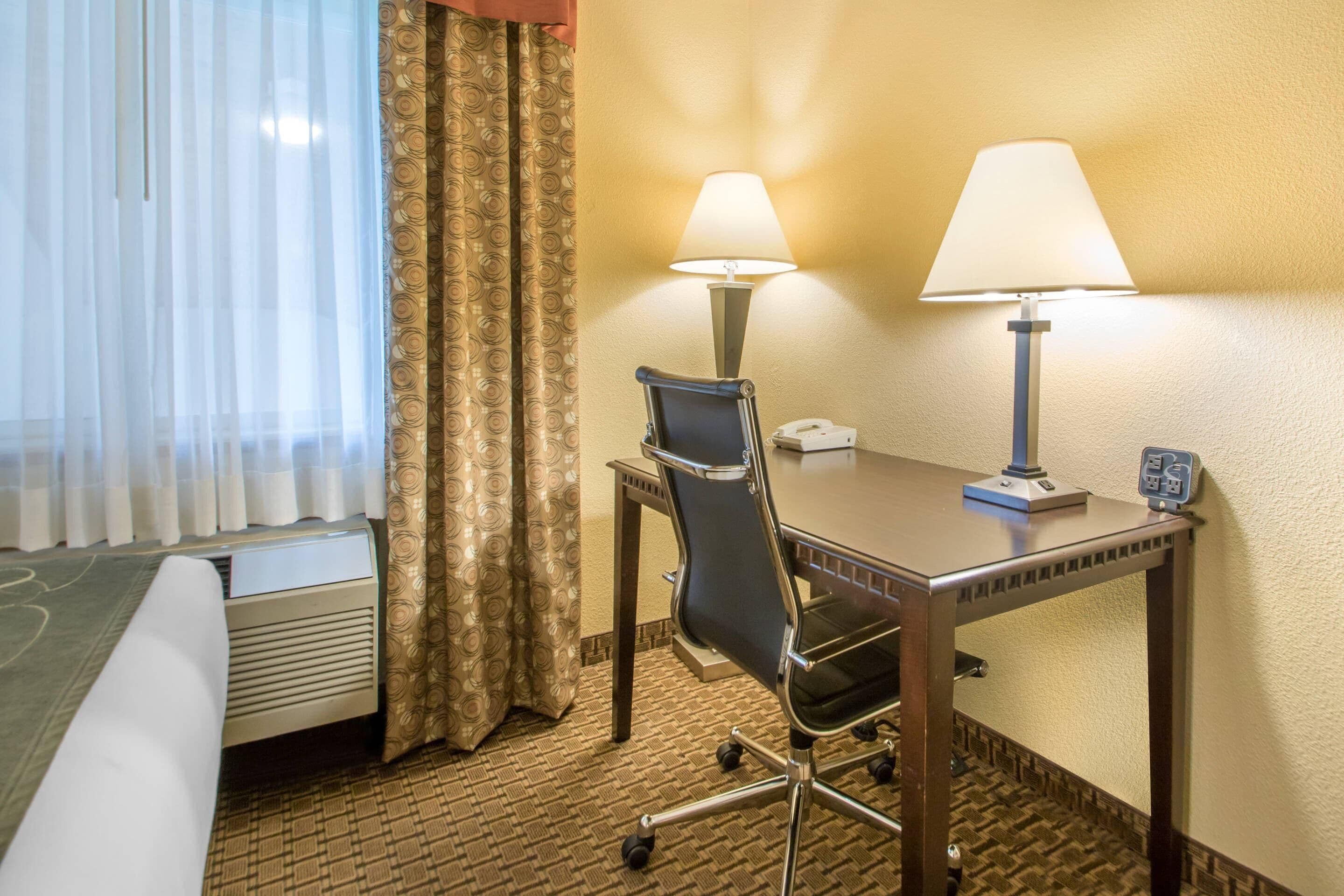 A hotel room with a bed, a desk with two lamps, a chair, and a telephone.