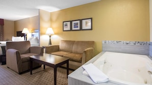 Une chambre d’hôtel avec un canapé, un fauteuil, une petite table, une grande baignoire et un tableau accroché au mur.
