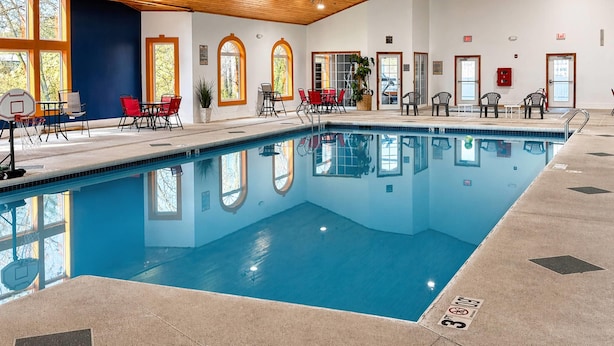 Une piscine intérieure à l’eau claire, entourée de chaises et de tables, et dotée de grandes fenêtres laissant entrer la lumière naturelle.