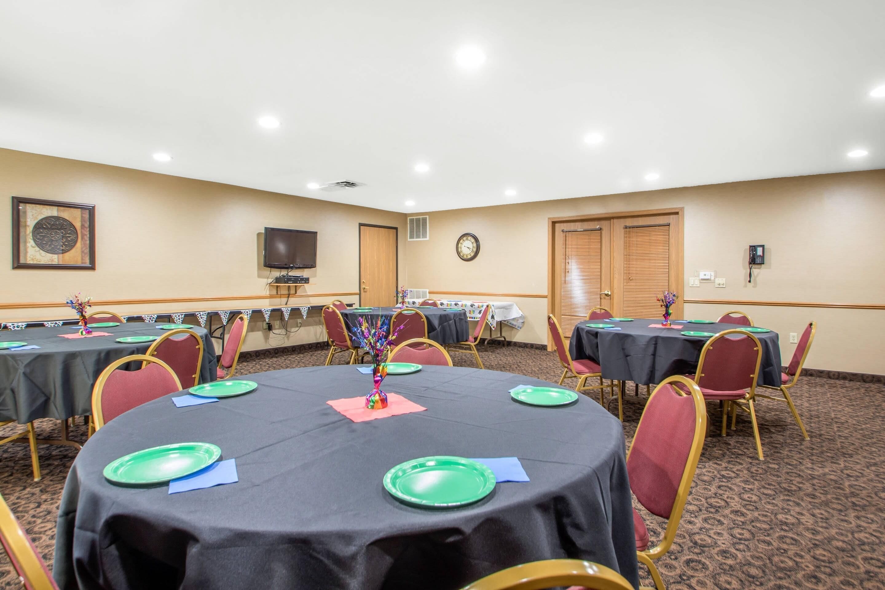 Une salle de conférence avec des tables rondes, des chaises et une horloge au mur.