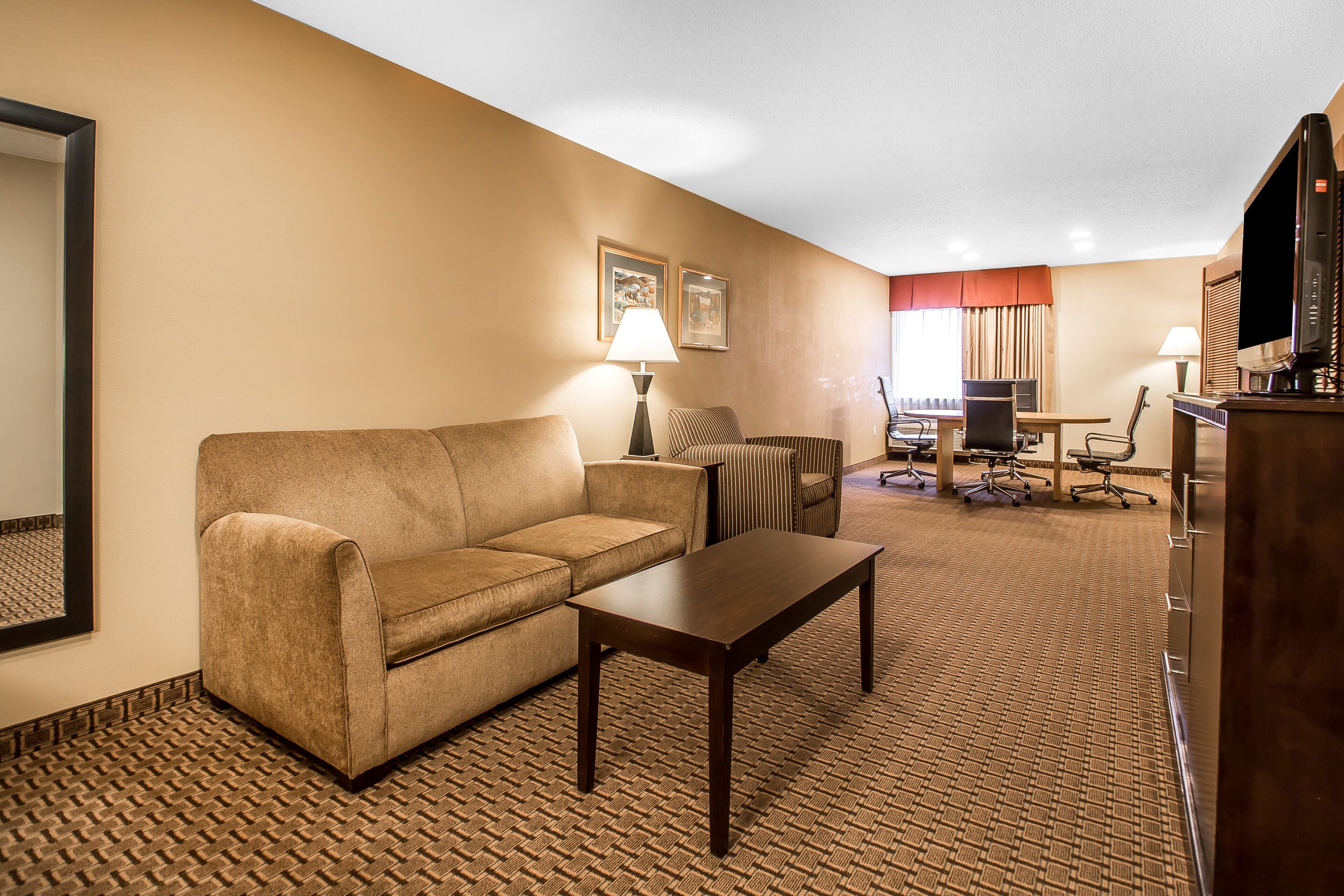 Una habitación de hotel con sofá, una mesita, un escritorio con silla, televisión y lámpara.