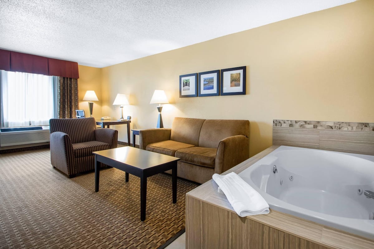 A hotel room with a sofa, armchair, small table, and a large bathtub.