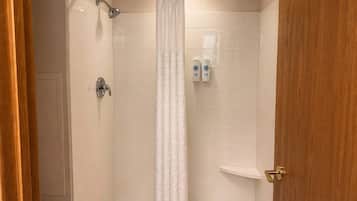 A shower with a white curtain, a handheld showerhead, and two bottles of shampoo on the wall.