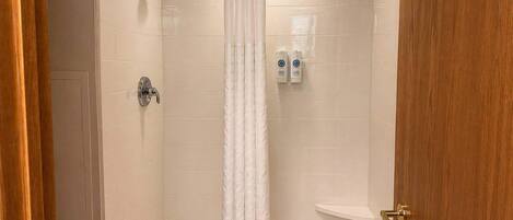 Une douche avec un rideau blanc, un pommeau de douche à main et deux bouteilles de shampoing accrochées au mur.