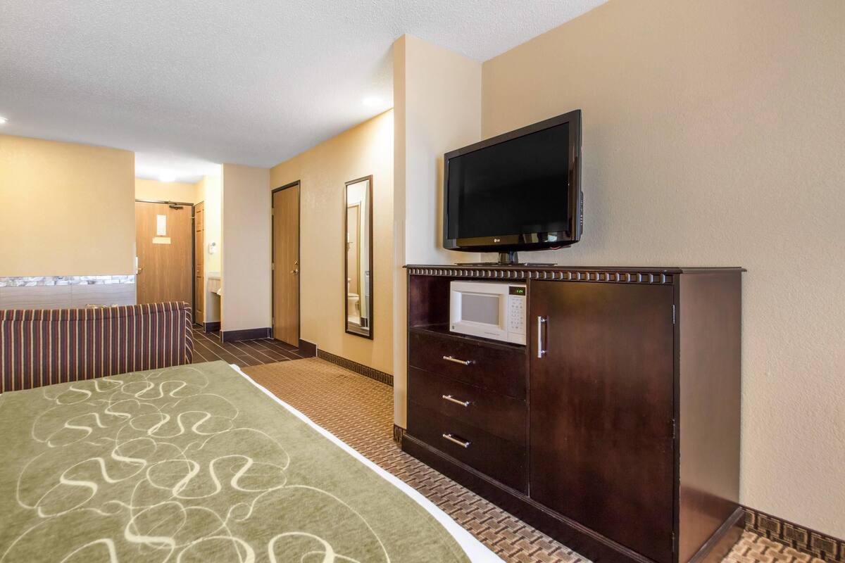 A hotel room with a bed, a television, a microwave, and a bathroom visible in the background.