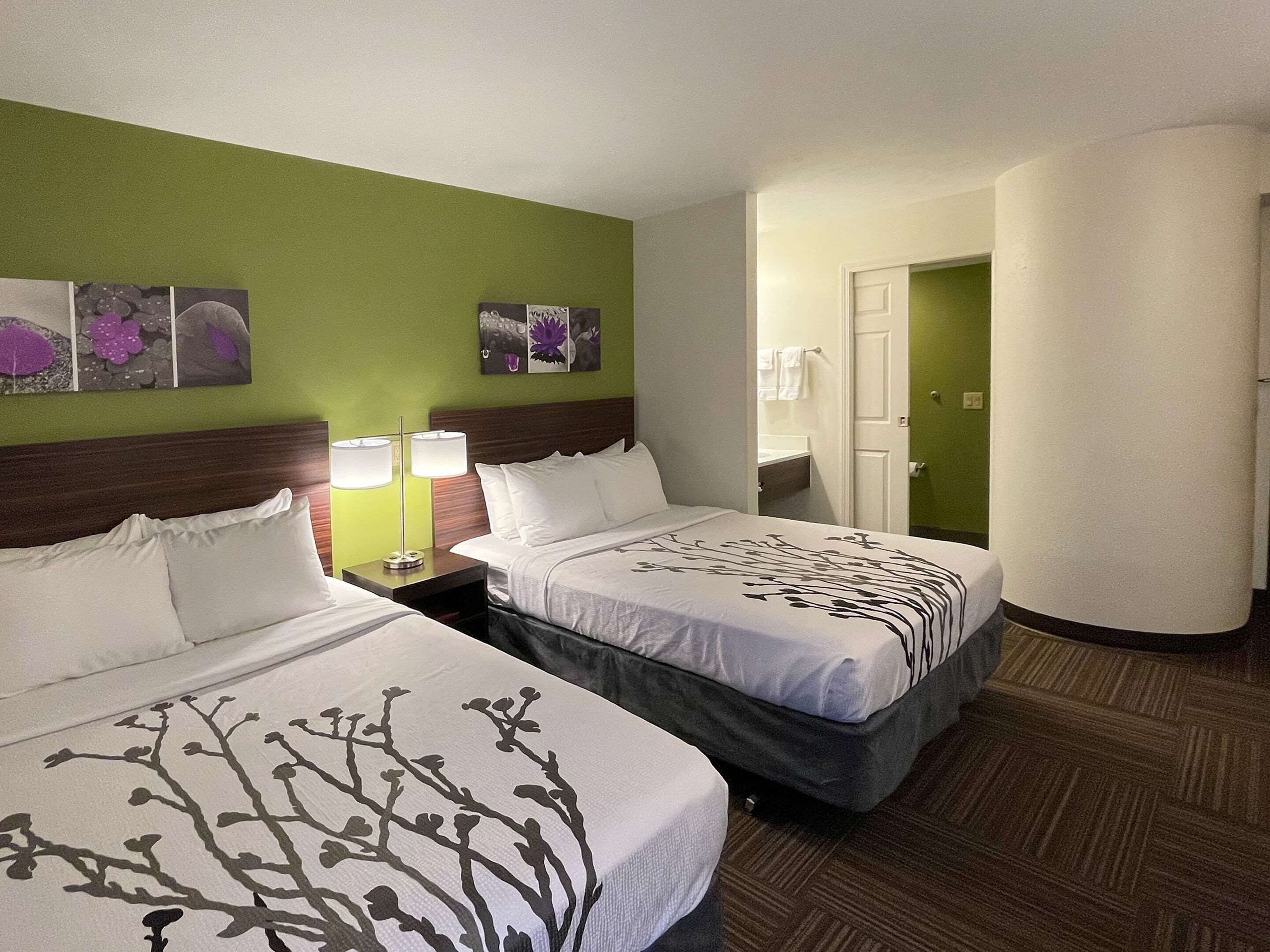 Quarto de hotel com duas camas, paredes verdes e obras de arte na parede.