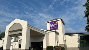 Un bâtiment de la chaîne Sleep Inn, qui fait partie du groupe Choice Hotels, avec une architecture moderne, caractérisé par une arche imposante à l'entrée et un ciel dégagé.