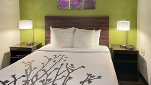 Une chambre d’hôtel comprenant un lit, deux tables de chevet, deux lampes et une œuvre d’art murale au-dessus du lit.
