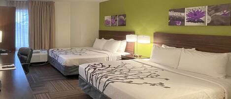 A hotel room with two beds, a desk, and a chair. There are wall art pieces and a window with curtains.