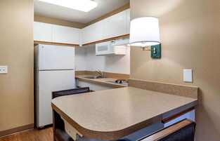 Una cocina compacta con gabinetes blancos, un microondas, un lavamanos y una encimera.