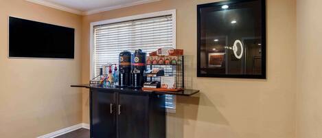 Una oficina en casa con un escritorio negro, un televisor de pantalla plana grande, una estación de café y un cuadro en la pared.