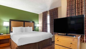 Ein Hotelzimmer mit einem großen Bett, einem Flachbildfernseher, hölzernen Nachttischen und Karottenvorhängen.