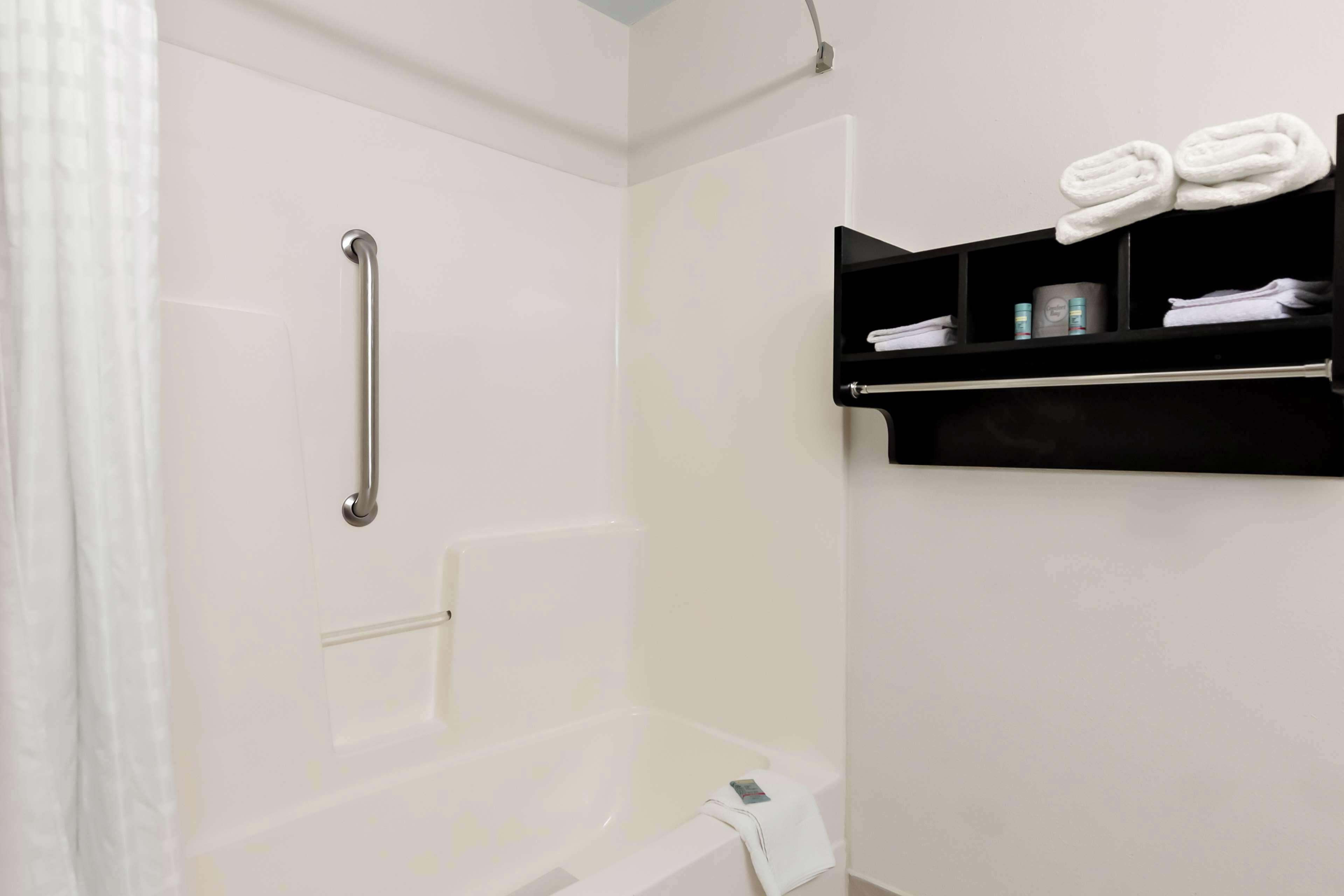 A bathroom with a shower, a grab bar, a towel rack with towels, and a shelf with toiletries.